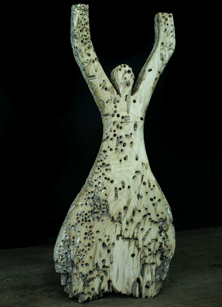 Scultura in legno riciclato raffigurante una donna che solleva le mano al cielo.